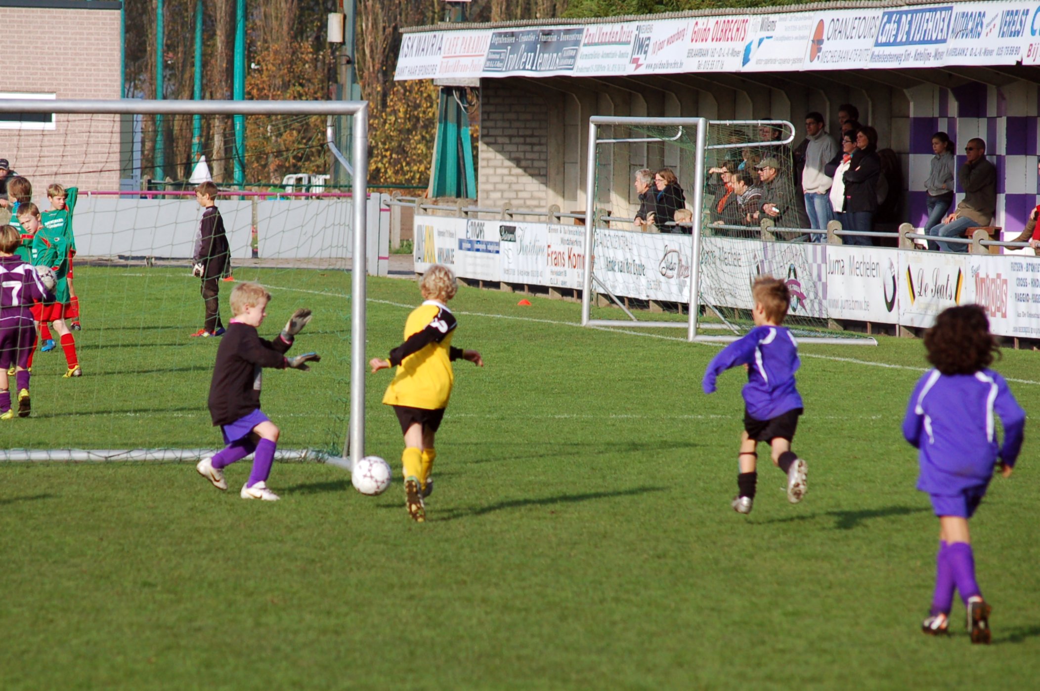 children playing soccer in a green field with spectators watching