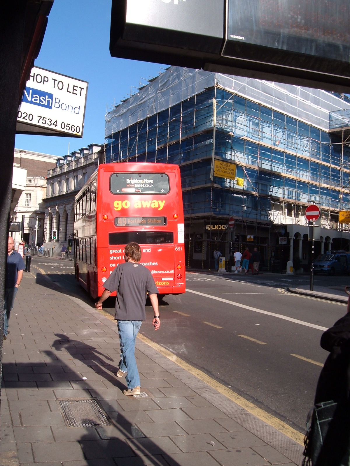 man walking down the sidewalk towards a large red bus