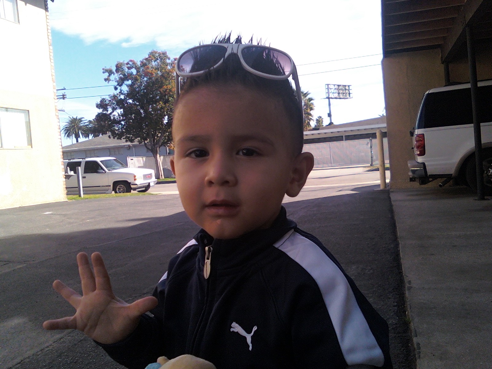 a boy wearing sunglasses stands near the side walk