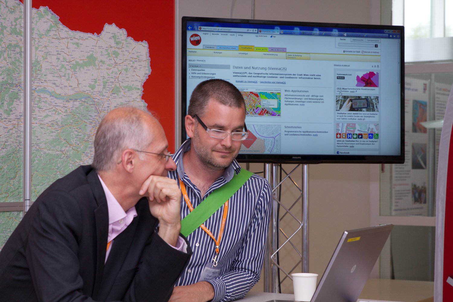 two men looking at a map while sitting in front of a laptop