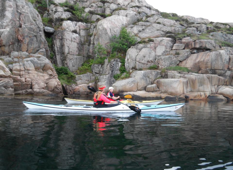 two people paddling a canoe on the water near large rocks