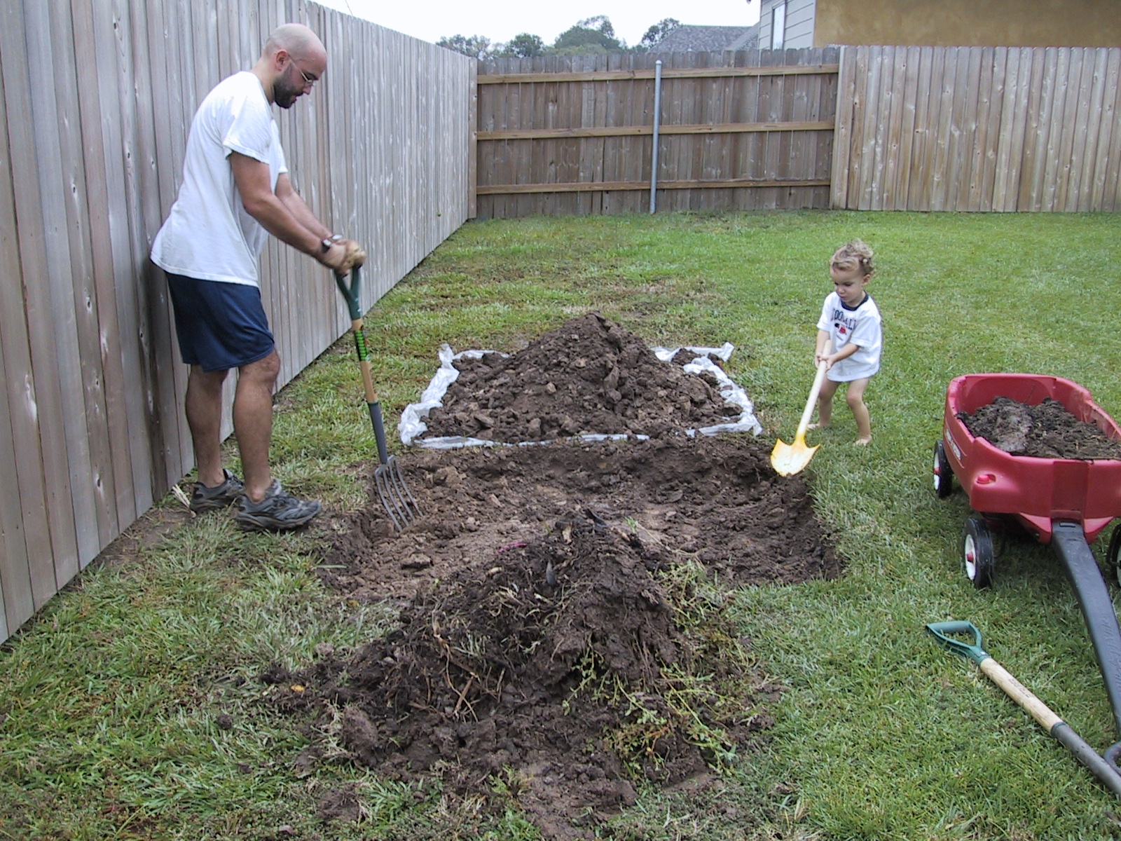 a man helping a little girl dig dirt into her backyard