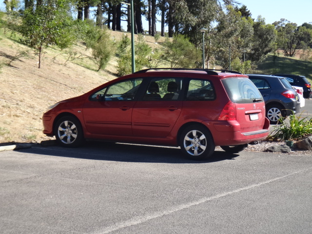 a red car parked on the side of a road near a hillside