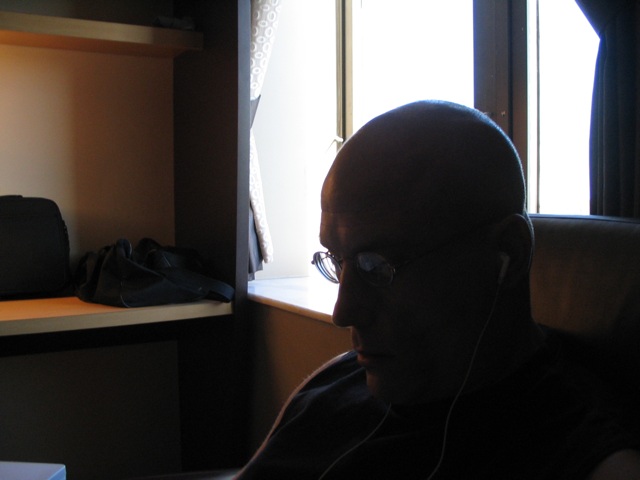 a bald man wearing glasses is looking out a window