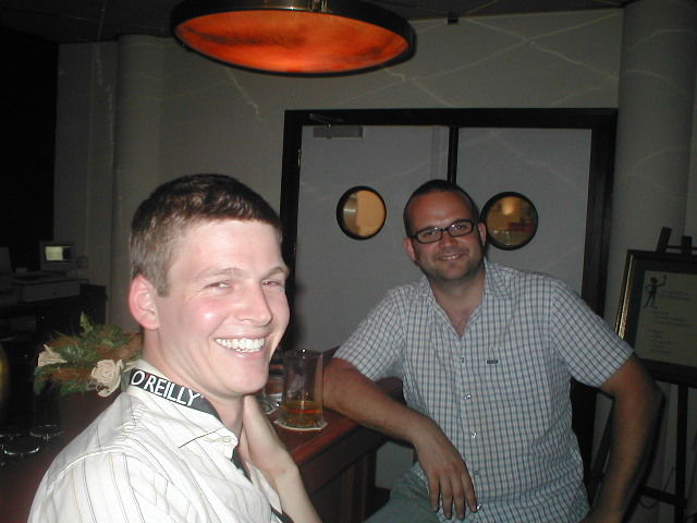man in a white shirt holding a glass of beer and another man with glasses smiling