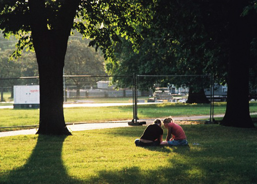 two people sitting down in the grass near a tree