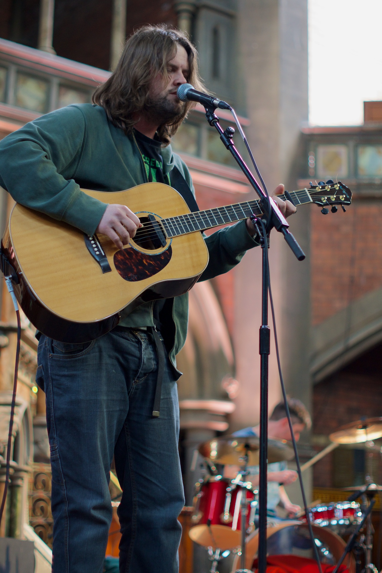 man playing guitar near a microphone and brick building