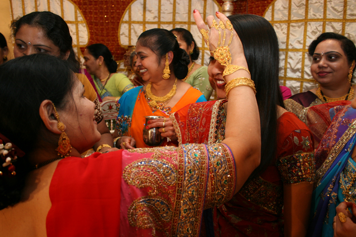 women in saris dressed up with jewels and a woman raising her hand