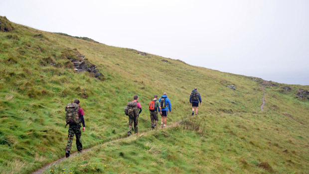 four people with backpacks hiking up a grassy hill