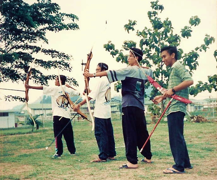 four young men, one holding two arrows and the other aiming with a bow