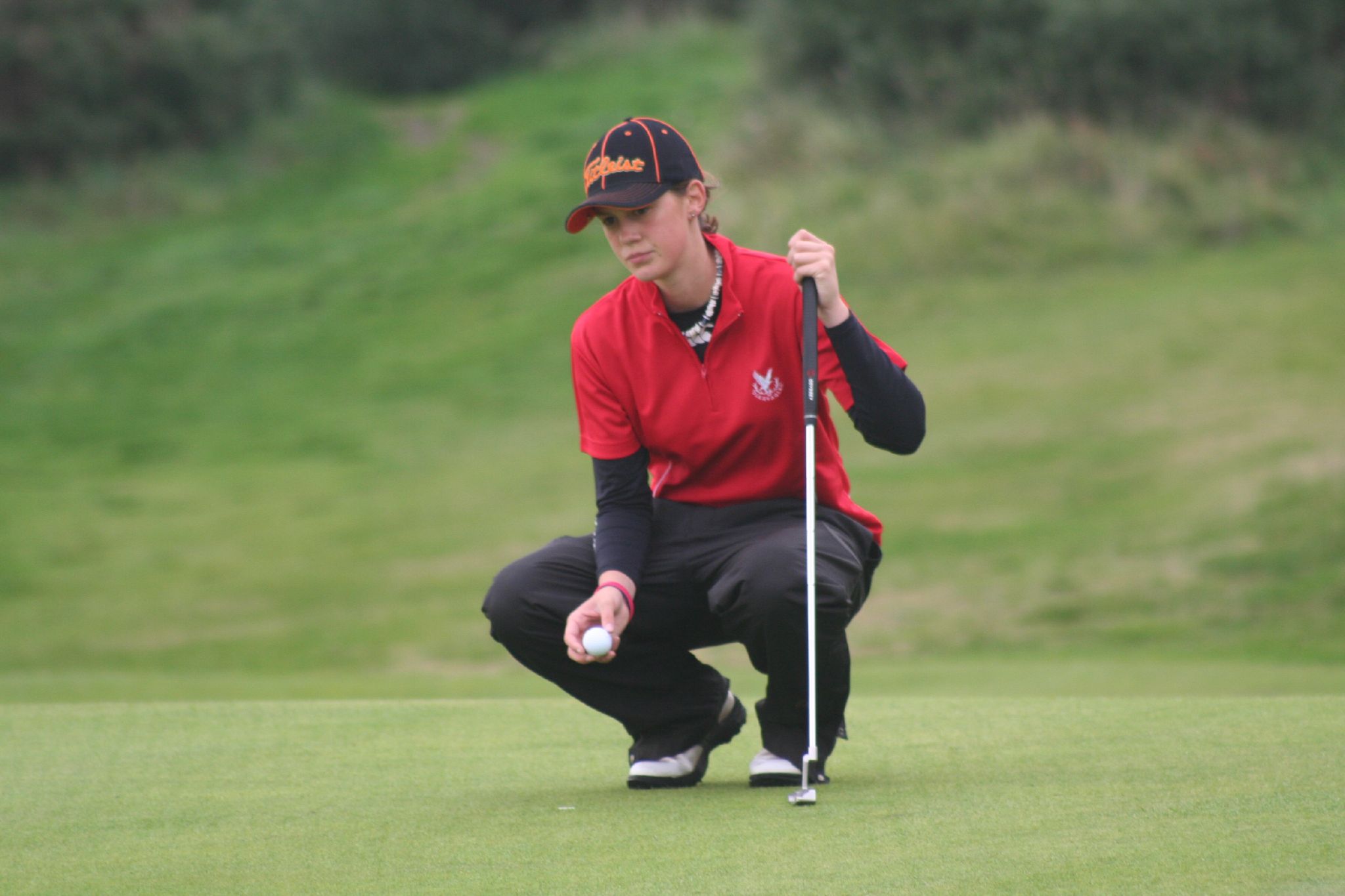 a golf player squats down and places his putter's ball on the green