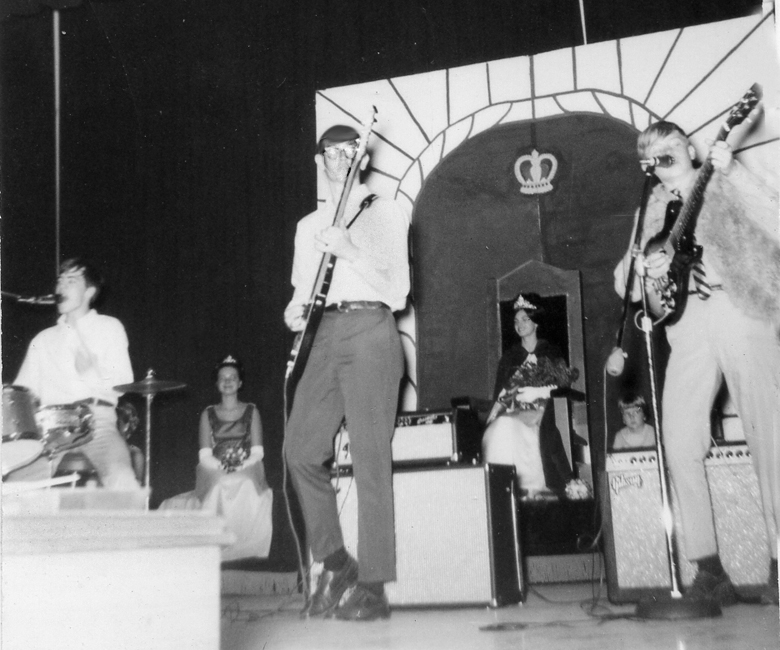 several people are standing on stage, one with a hat and holding instruments