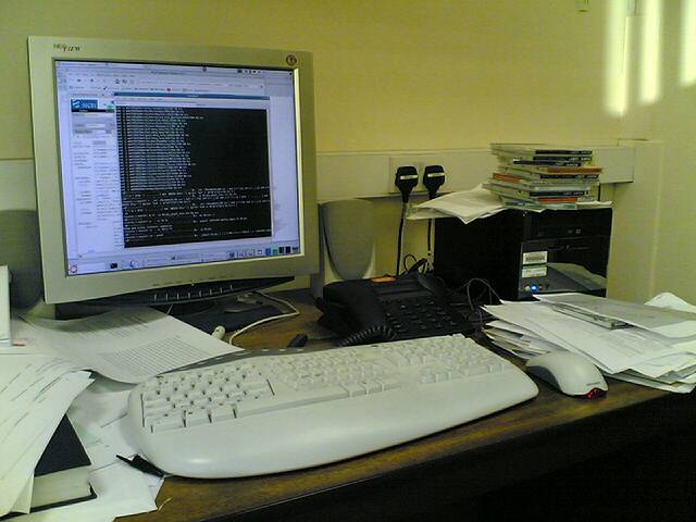 a cluttered desk with a keyboard, mouse and monitor