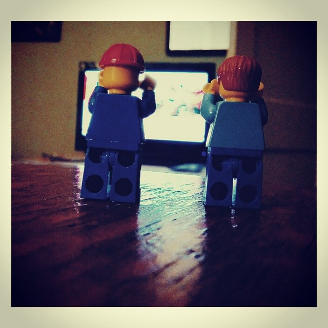two lego man holding up their hands in front of the television
