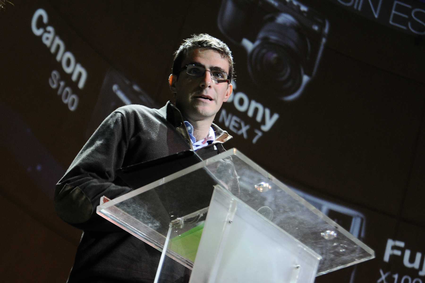 a man standing at a podium with a camera behind him