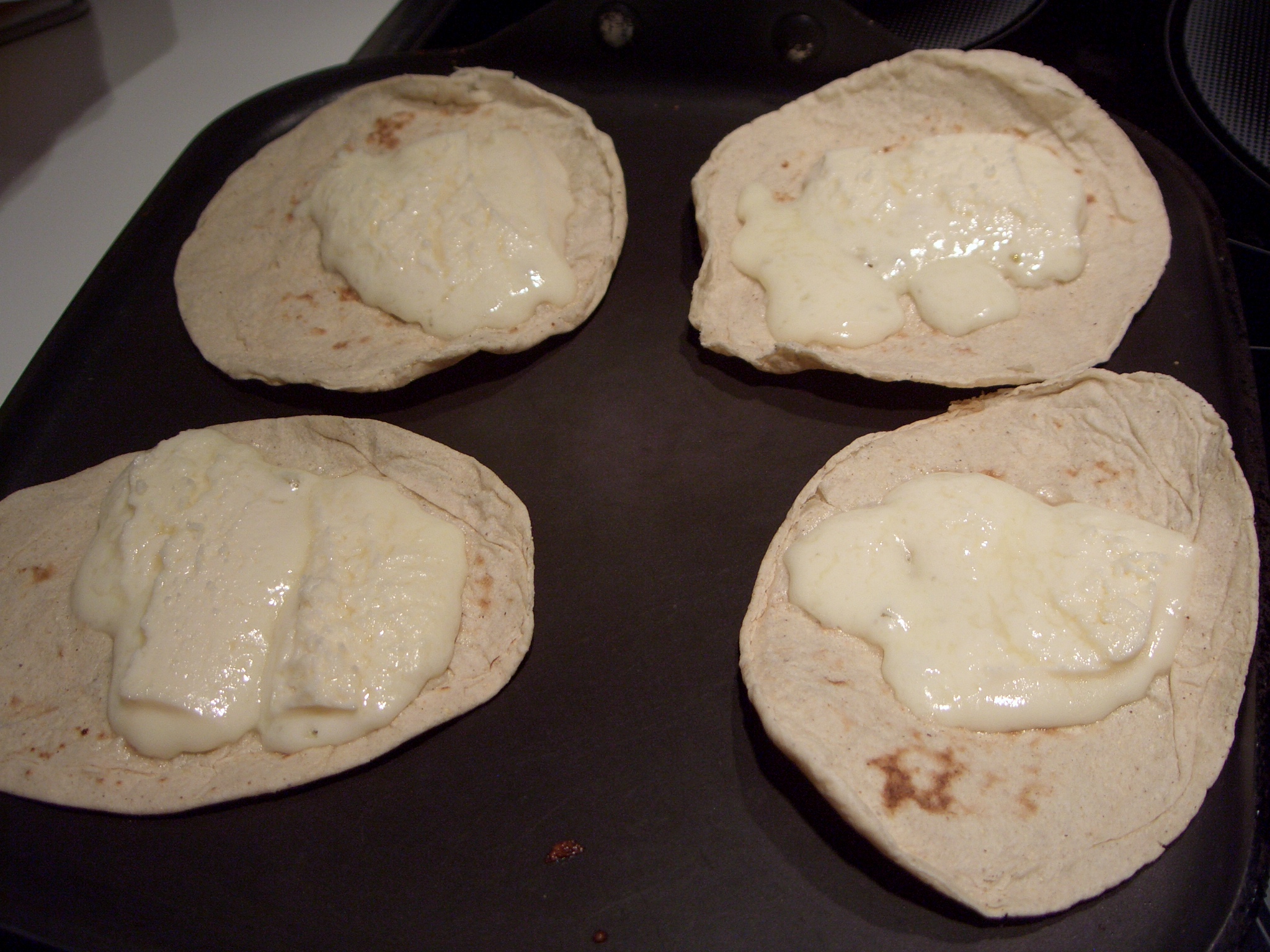 four pita breads covered in cheese sit on top of a black plate