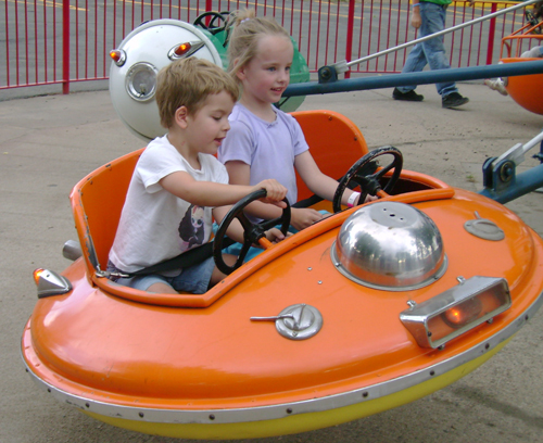 two children in an orange pedal car at a carnival
