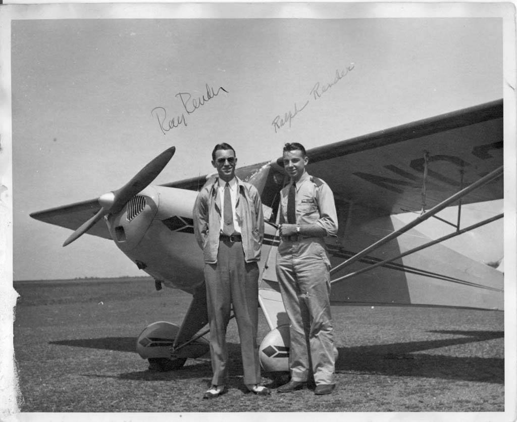 two men posing next to an old fashioned airplane