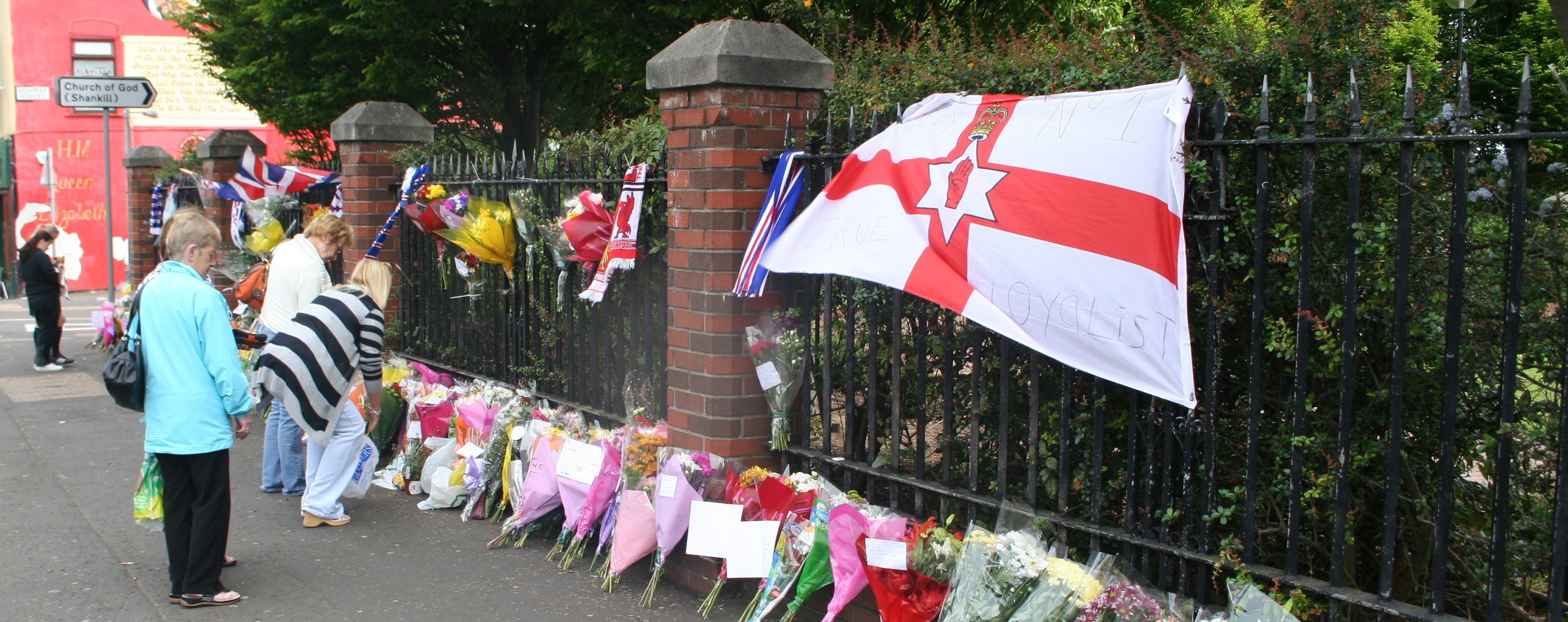 flags and flowers are tied to the fence at an rememnce site