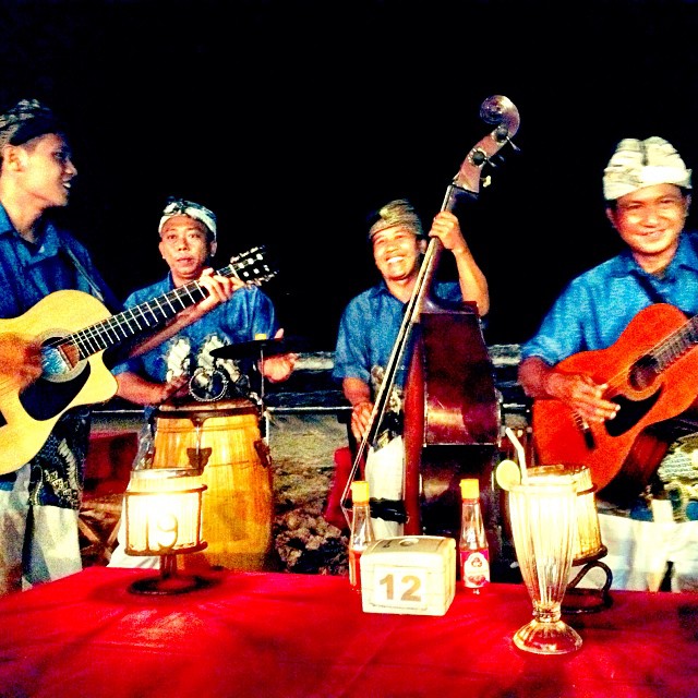 three men are sitting and playing guitars at a table