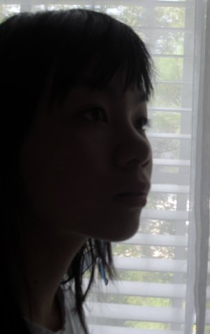 young asian woman staring out of window in the dark