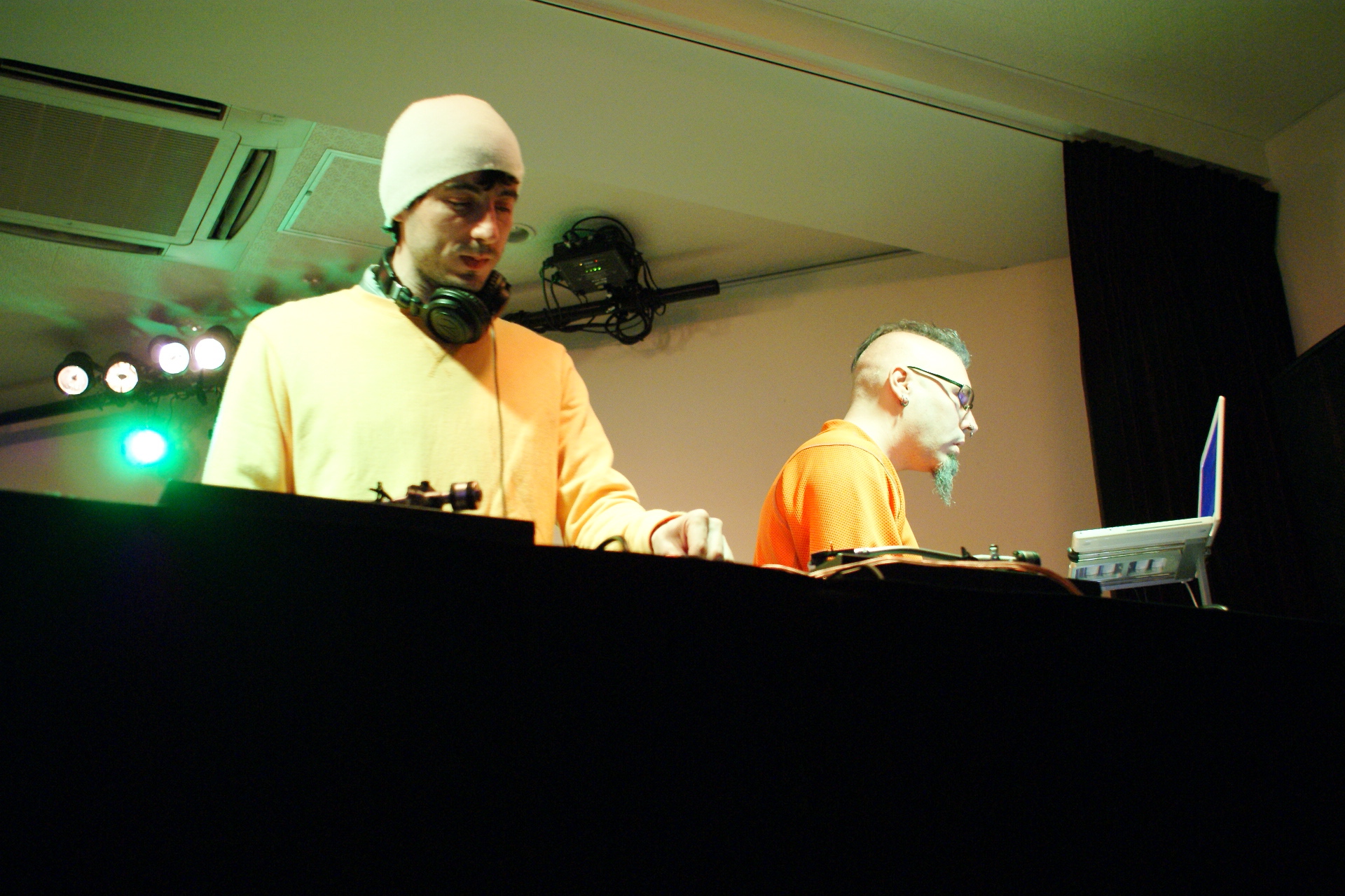 two male djs in bright orange shirts and headphones