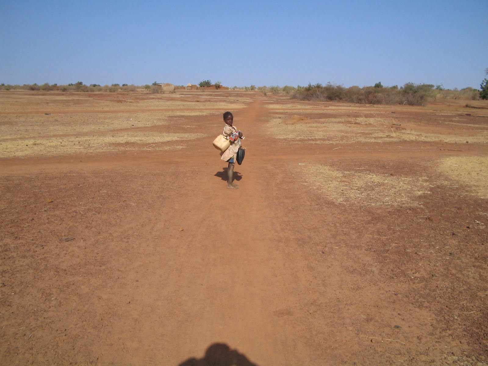 a man running across a dirt road carrying a suitcase