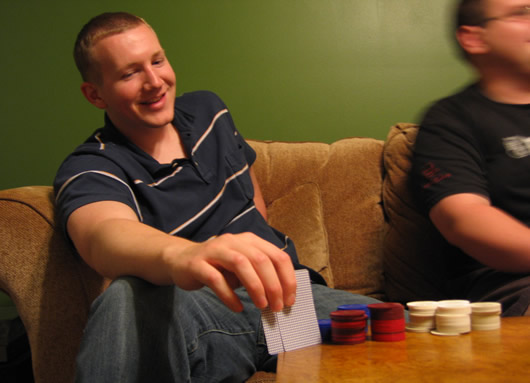two men sitting on a brown couch playing a game of unopened cards