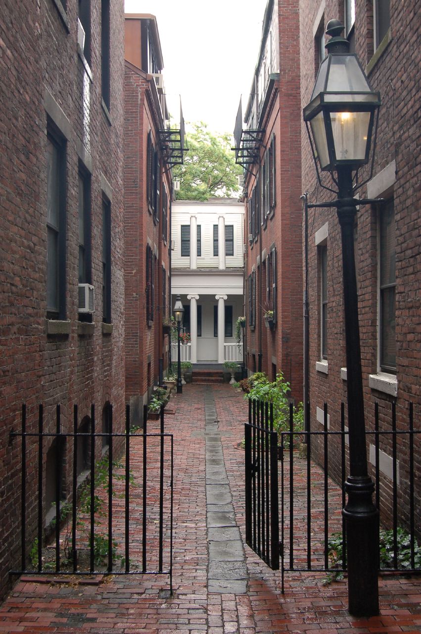 the alleyway between two brick buildings has a wrought iron gate