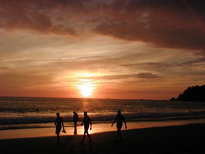 several people walk along a beach as the sun sets