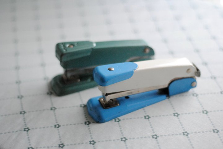 two plastic blue and green staplers on top of paper