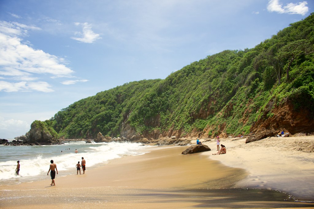 people walking on the beach near a cliff