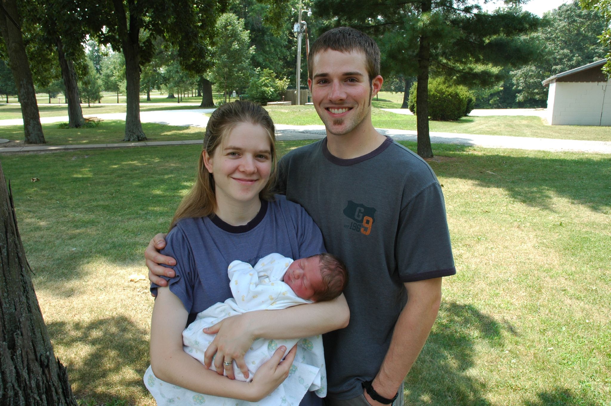 a man and woman holding their newborn in a park
