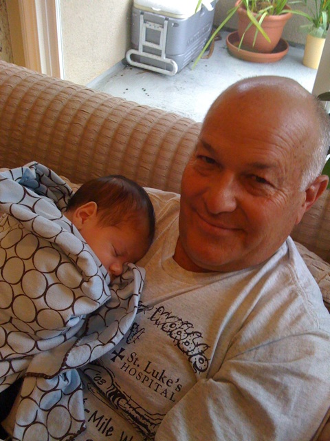 a bald man is sitting on a couch holding a sleeping baby