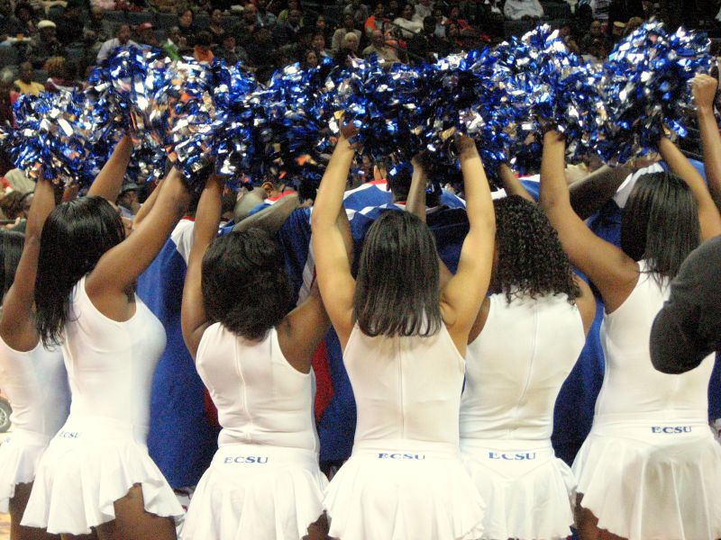 a group of women wearing cheerleader uniforms stand in a gym holding onto poms