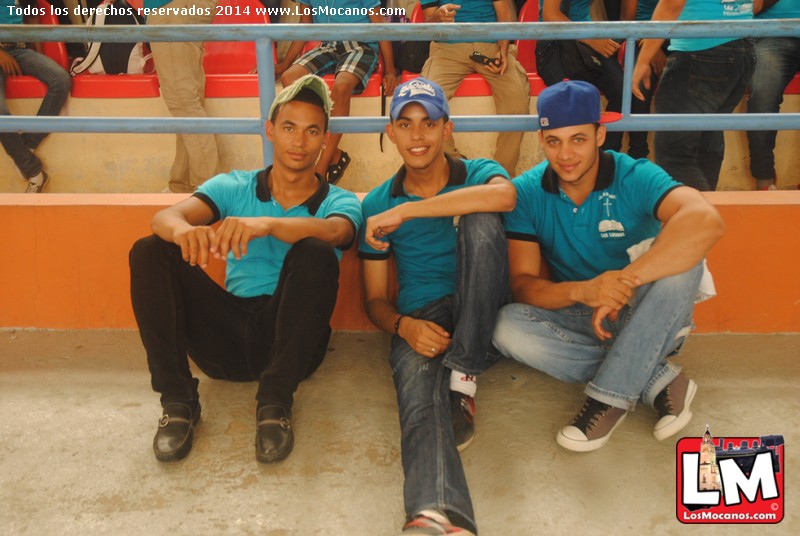 three men posing in the bleachers at a baseball game