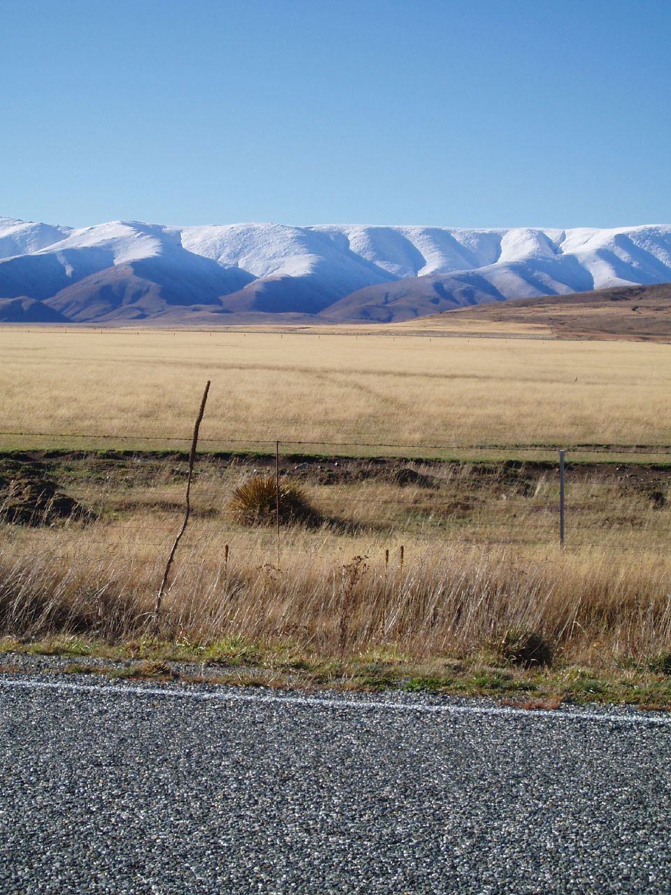 a road with a car approaching by snow capped mountains in the distance