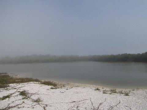 a body of water sitting on the side of a fog covered mountain