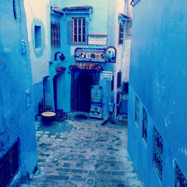 a narrow street between two blue buildings and other buildings