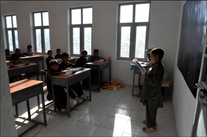 a classroom full of students with desks and one boy reading a book