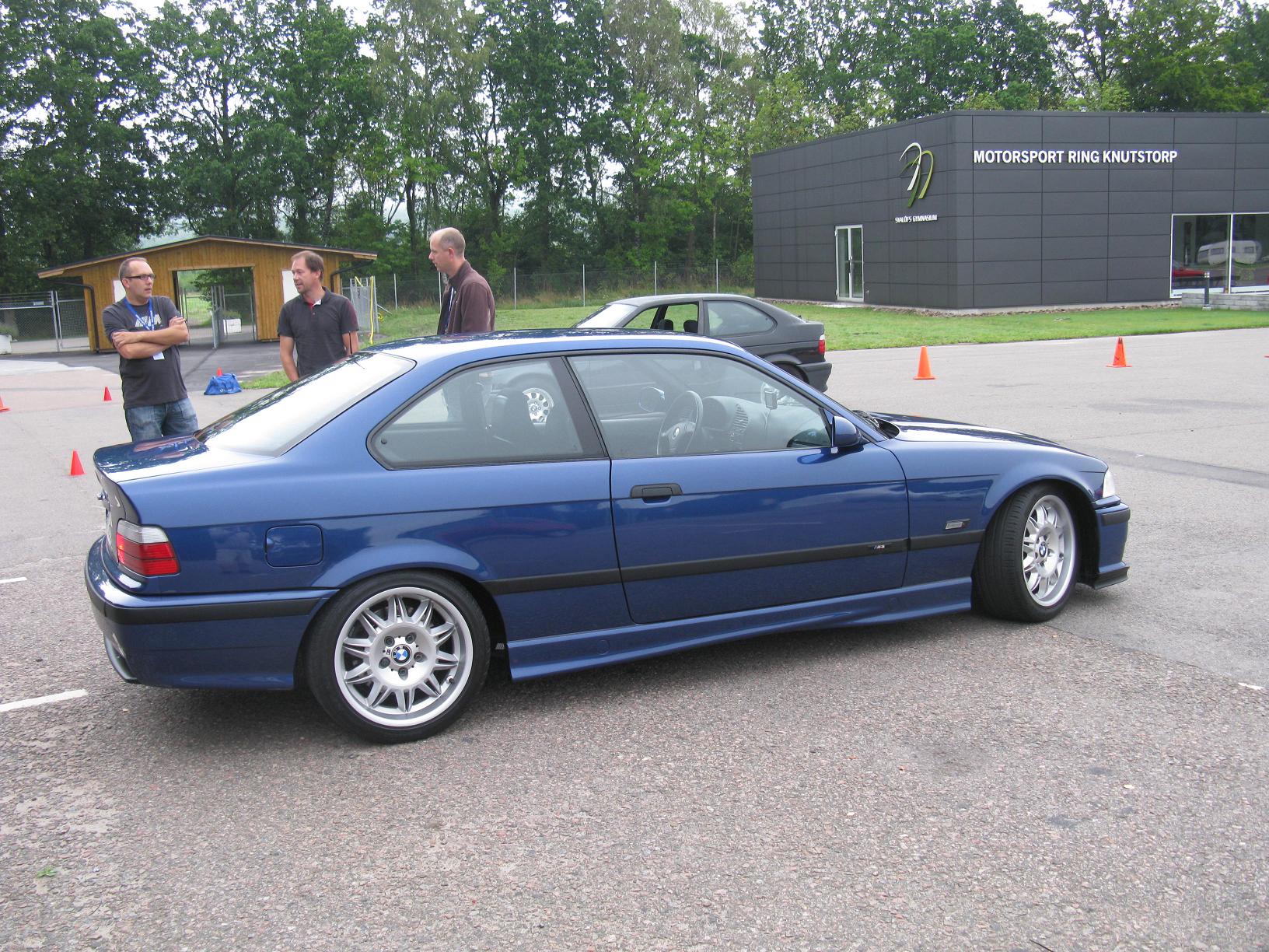 the three people are standing next to the parked bmw