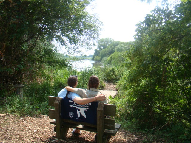 two people are sitting on a bench by a river