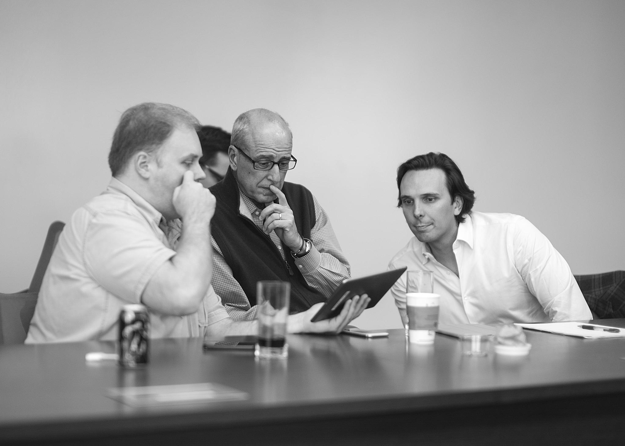 three men at a table looking over paper on a clipboard