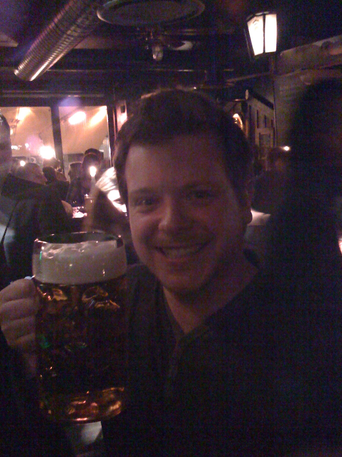 man smiling at the camera while holding up a glass of beer