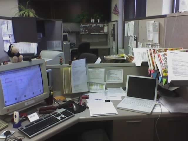 a view of office cubicle with various papers and electronic devices on the desk