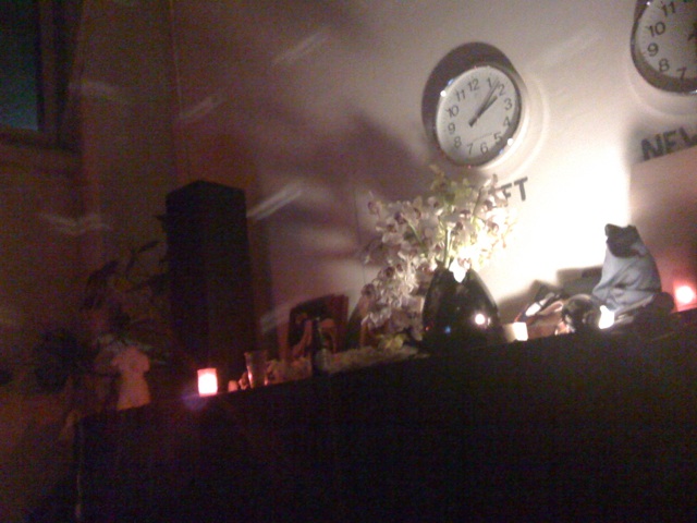 a set of three clocks mounted to a wall above some candles