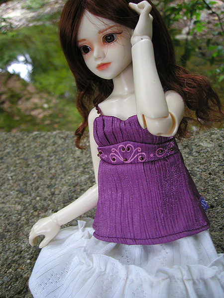 a doll wearing a purple dress holding a finger up in front of her head