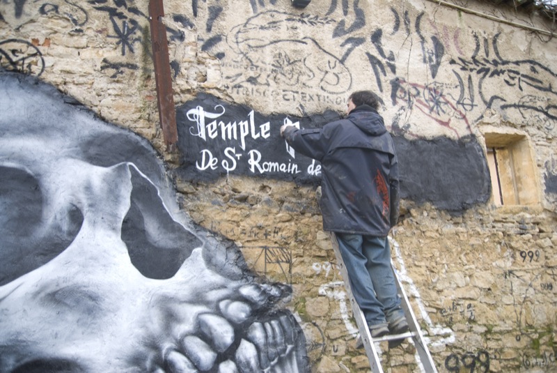 a man painting on the wall with skull heads