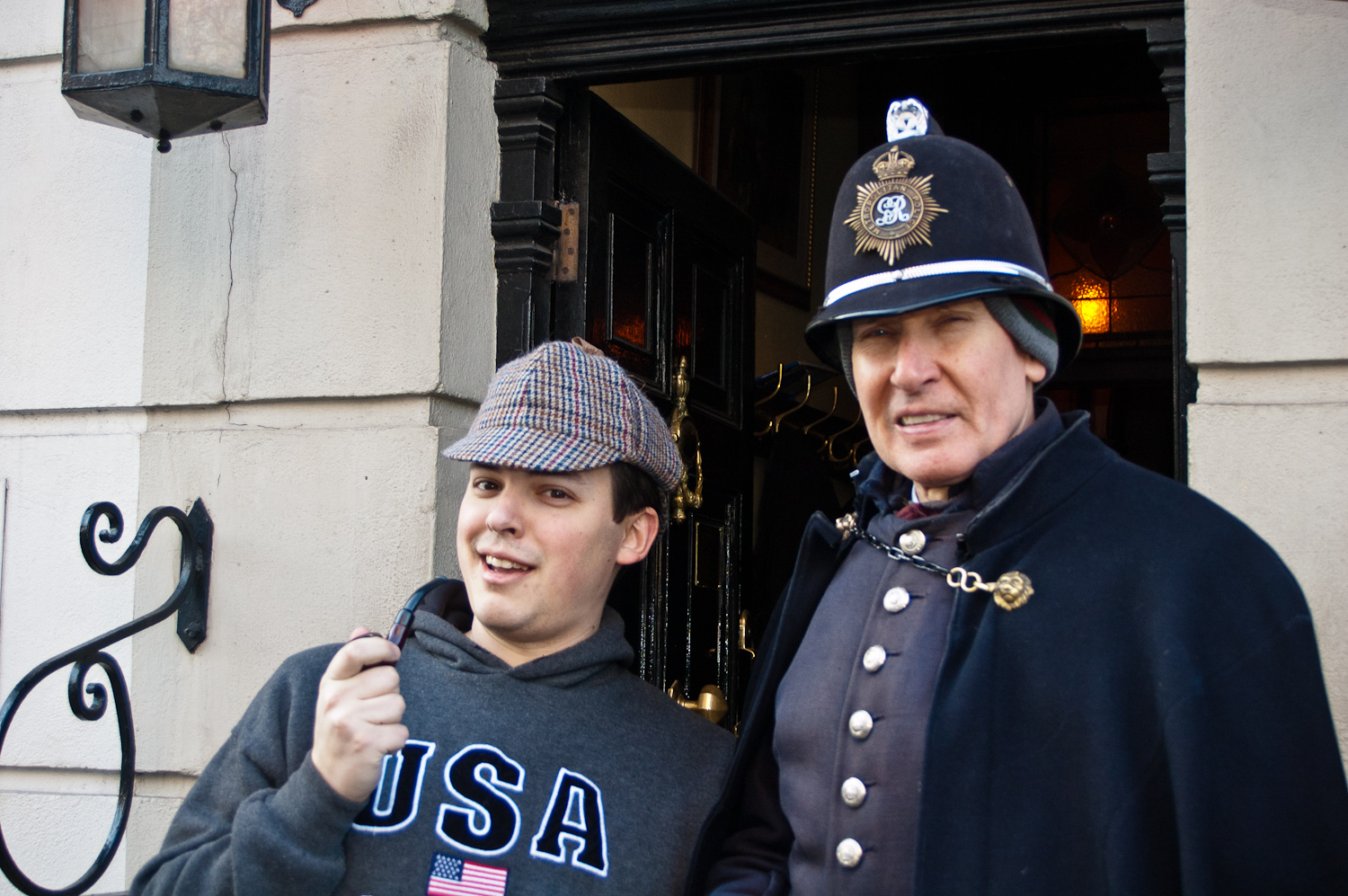 two people wearing coats and hats pose in front of a building