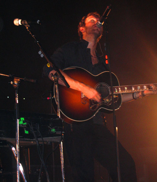 a man standing at the microphone with an acoustic guitar